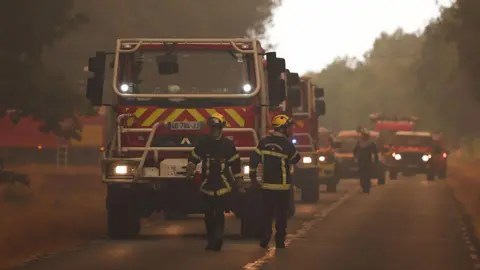 AFP via Getty Images Lines of fire trucks on a road with hazy smoke in the air